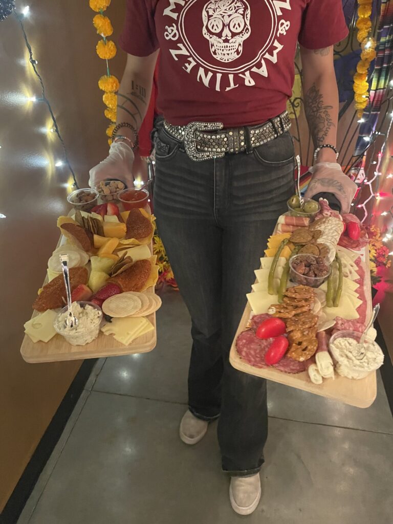Person holding two charcuterie boards with snacks.