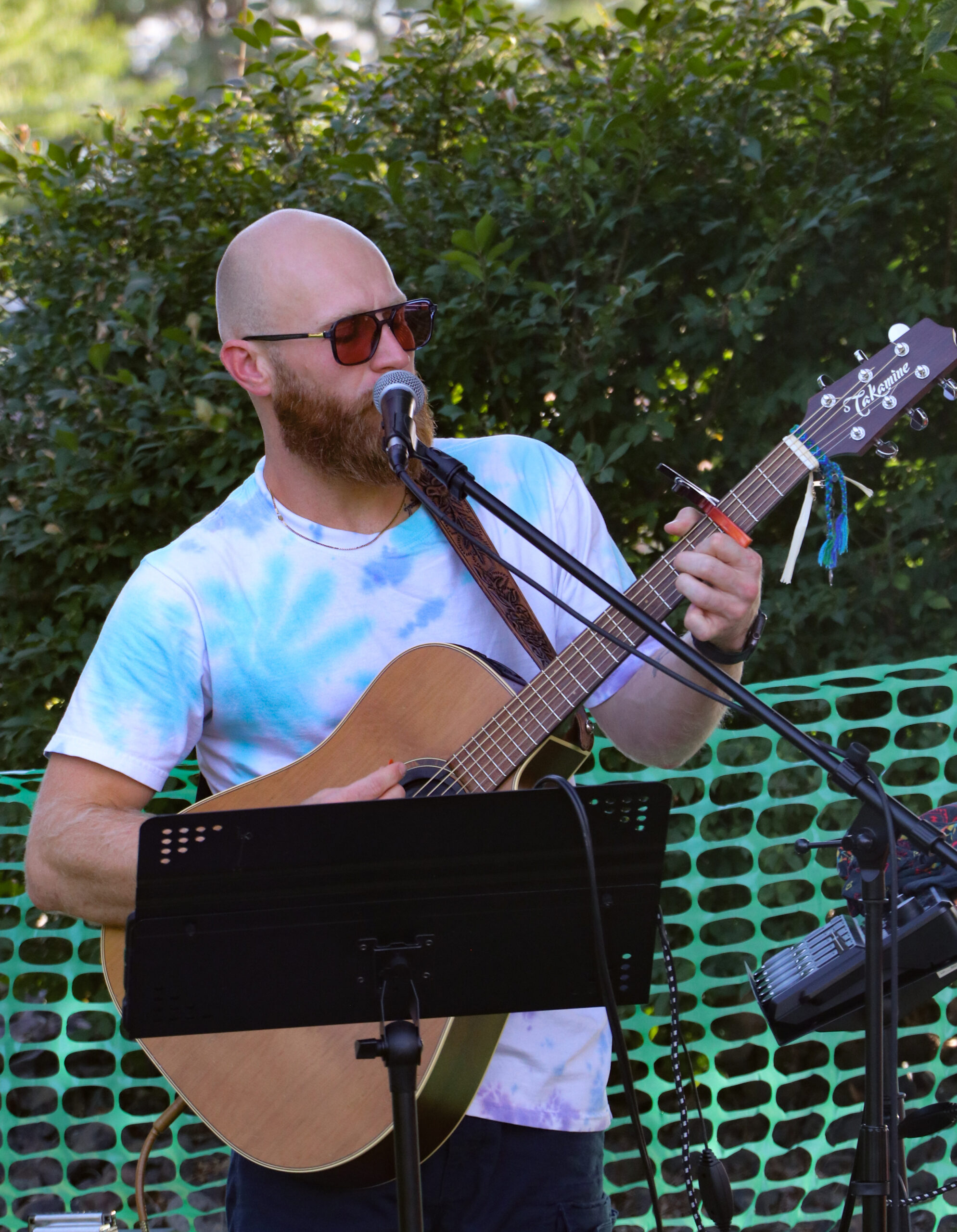 Musician playing guitar outdoors with microphone.