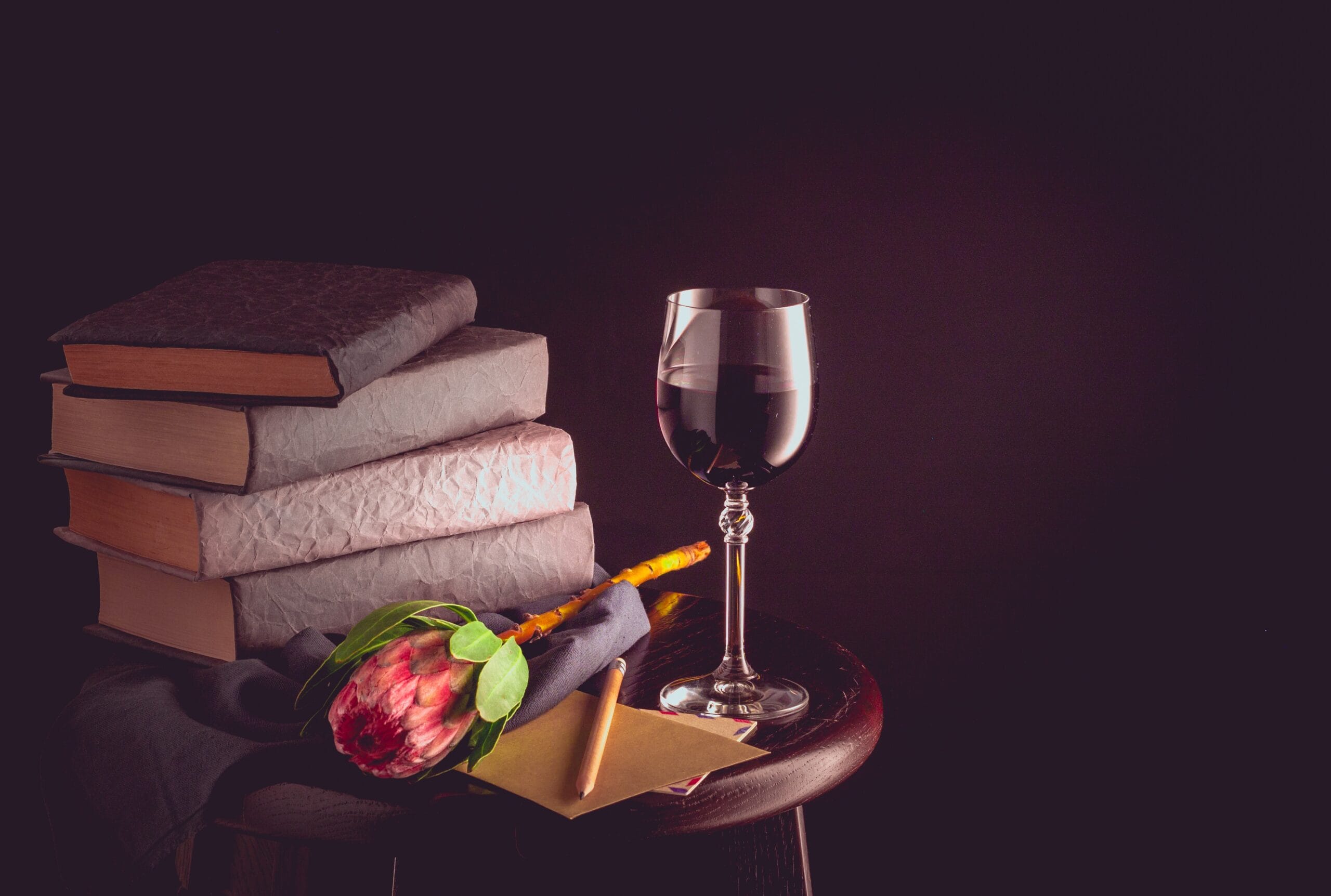 Wine glass, books, flower, and envelope on table.