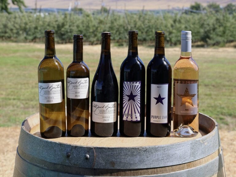 Variety of wine bottles on a wooden barrel outdoors.