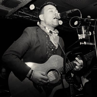 Musician performing on stage with acoustic guitar.