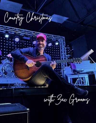 Man playing guitar on stage with festive lights.