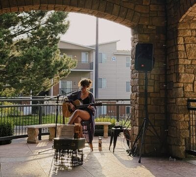 Woman playing guitar at outdoor venue, sunny afternoon.