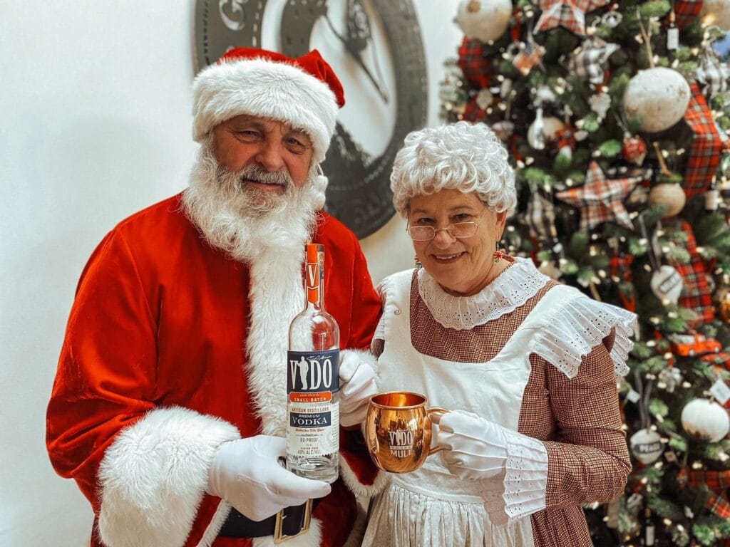 Santa and Mrs. Claus by Christmas tree with drinks.