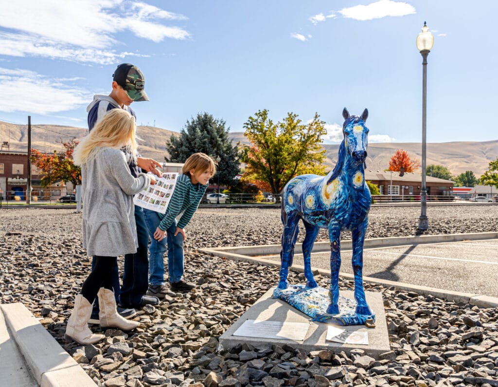Children examining painted blue horse sculpture outdoors.