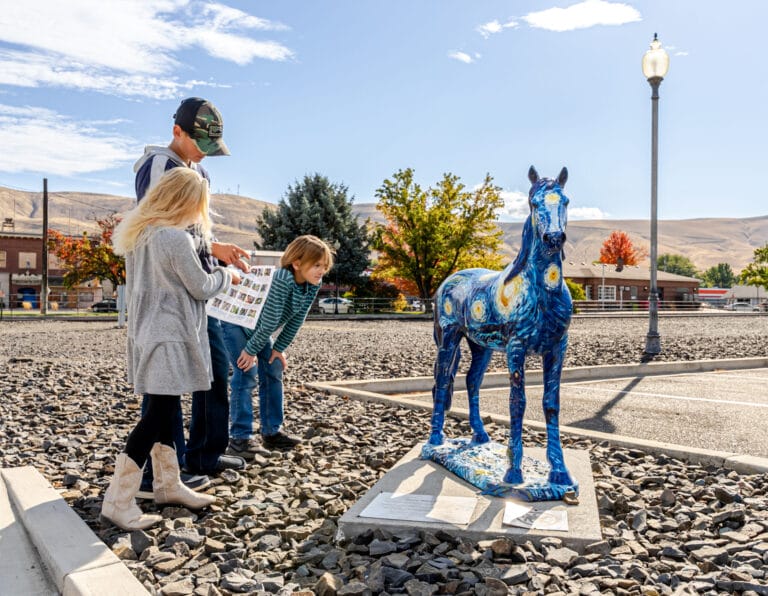 Children examining painted blue horse sculpture outdoors.
