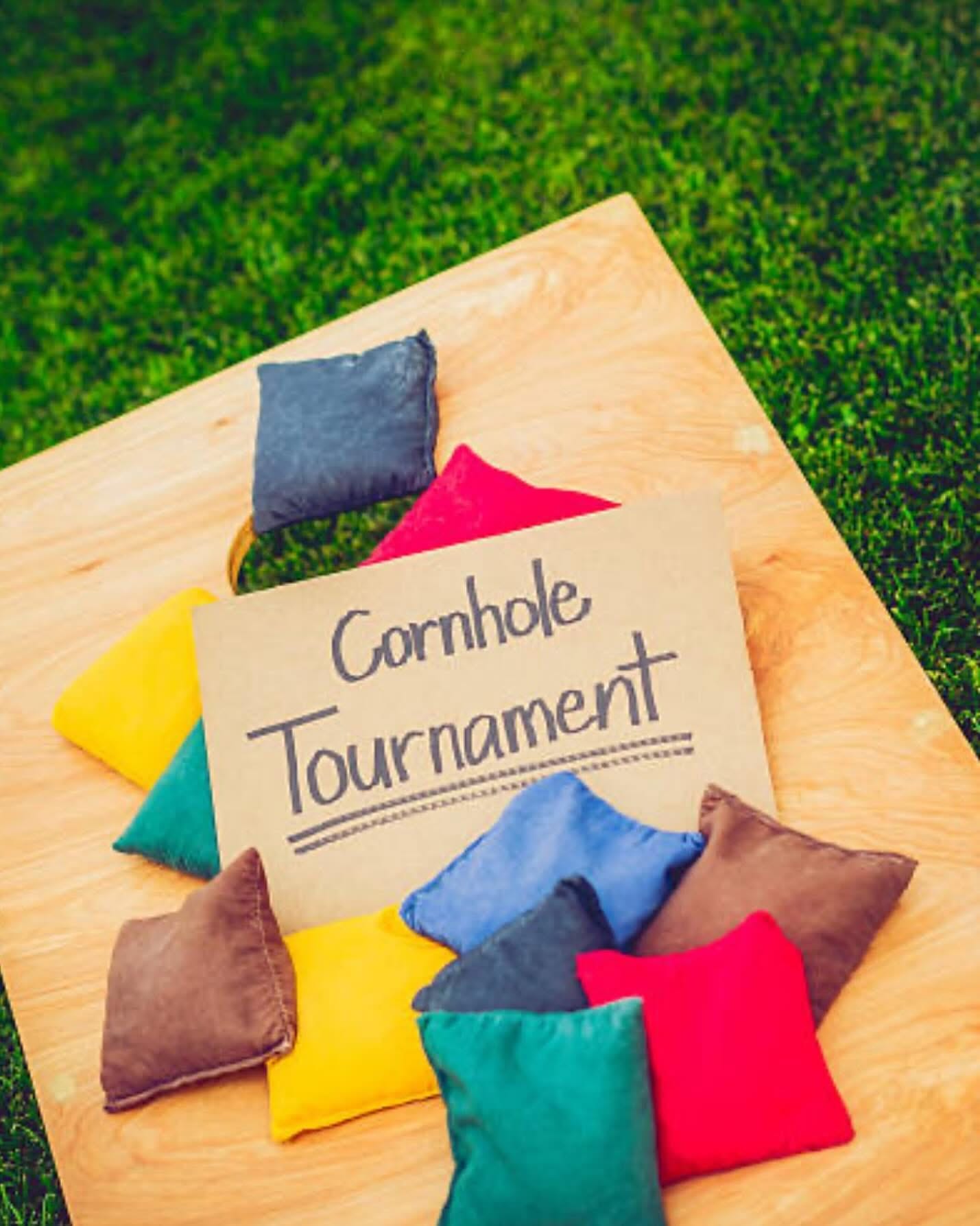 Colorful cornhole bags with tournament sign on grass.
