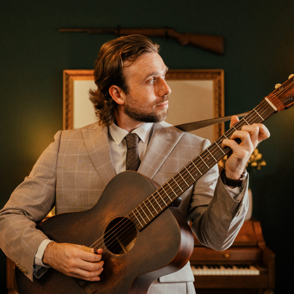 Man in suit playing acoustic guitar indoors.
