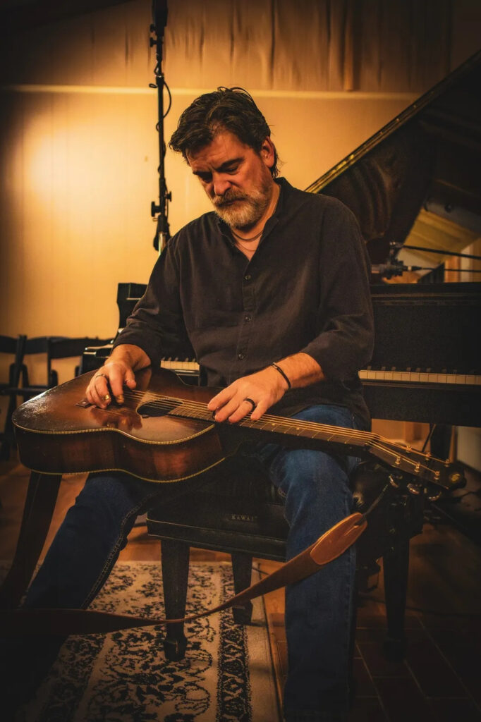 Man playing acoustic guitar in cozy studio setting.