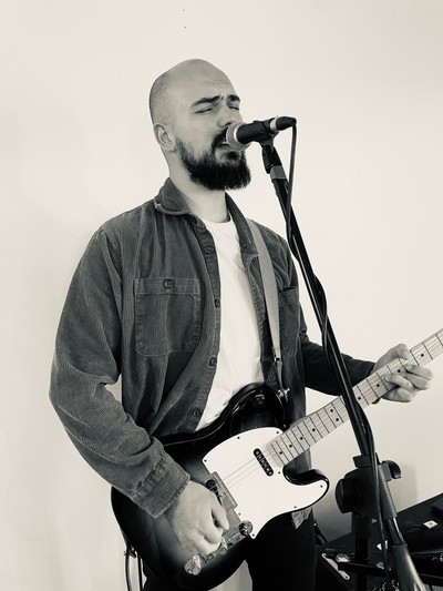 Musician singing and playing electric guitar on stage.