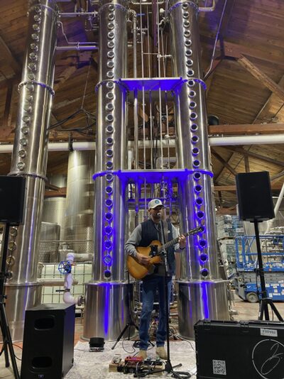 Musician playing guitar in an industrial distillery setting.