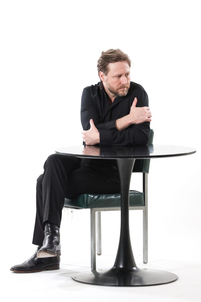 Man in black outfit sits at round table.