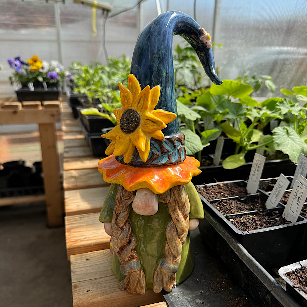 Ceramic gnome with sunflower hat in greenhouse.