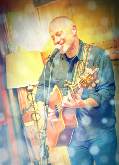 Man playing acoustic guitar and singing on stage.