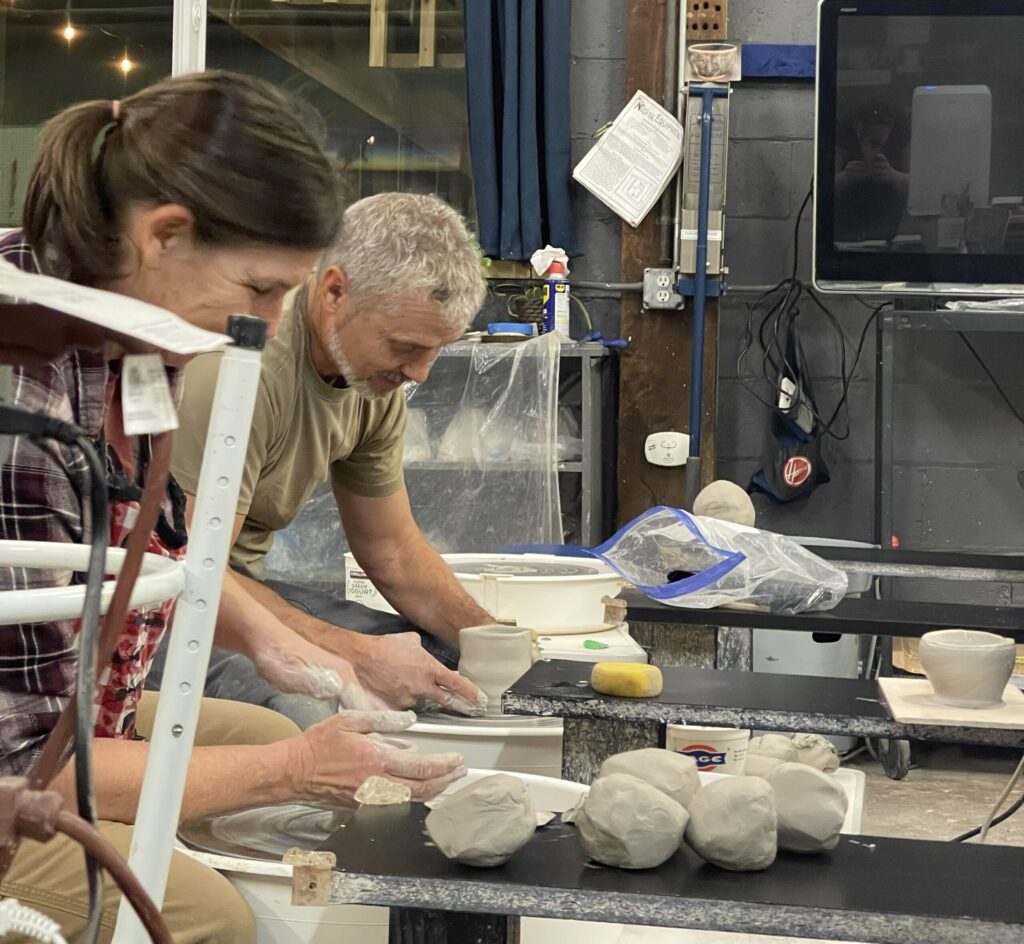 Two people crafting pottery on wheels.