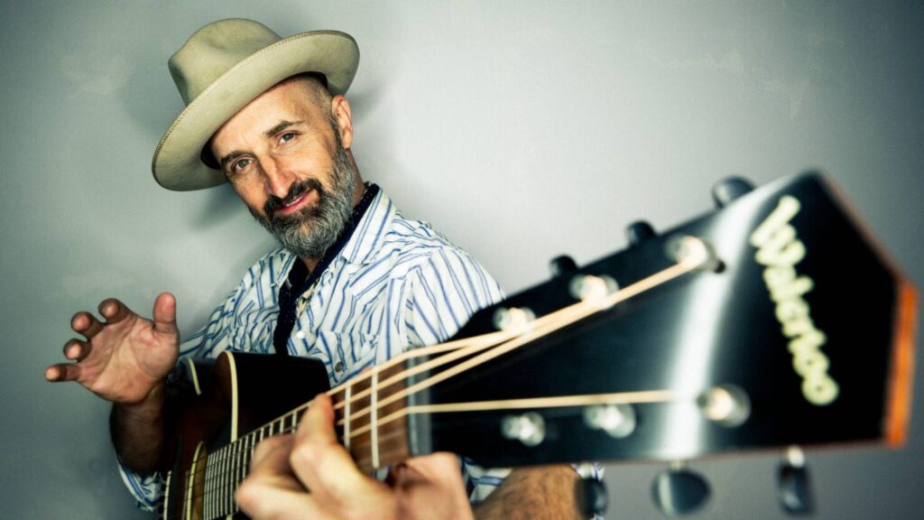 Bearded man playing acoustic guitar in hat