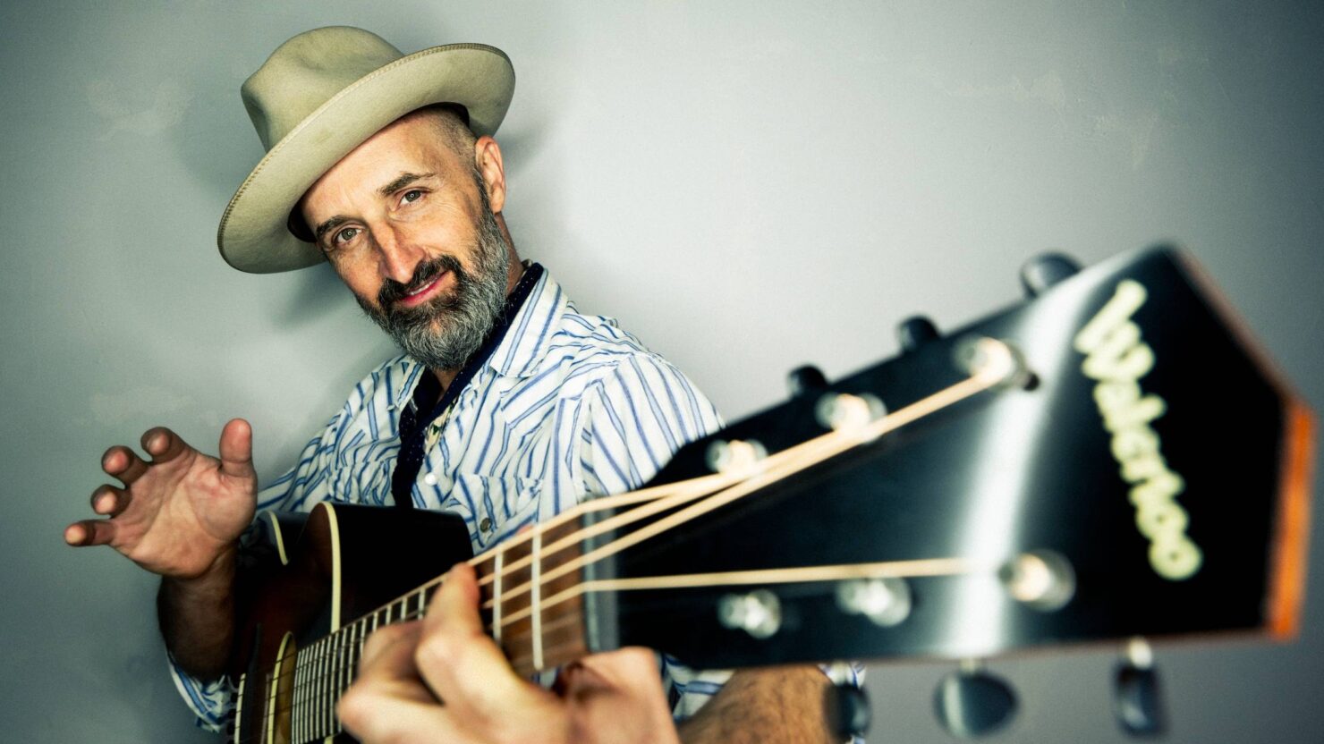 Bearded man playing acoustic guitar in hat