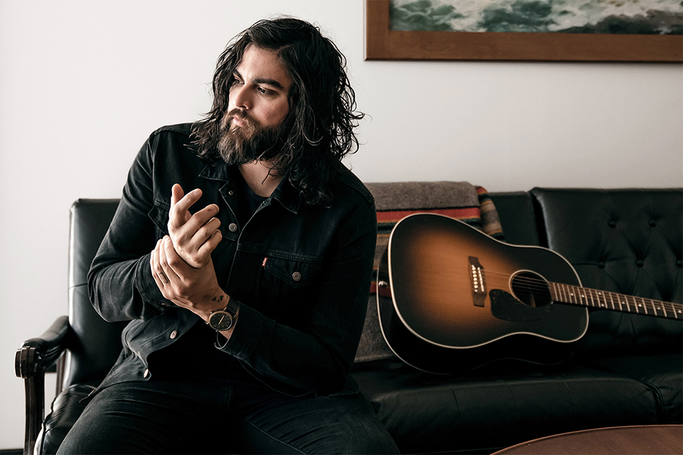 Bearded man beside acoustic guitar on leather couch