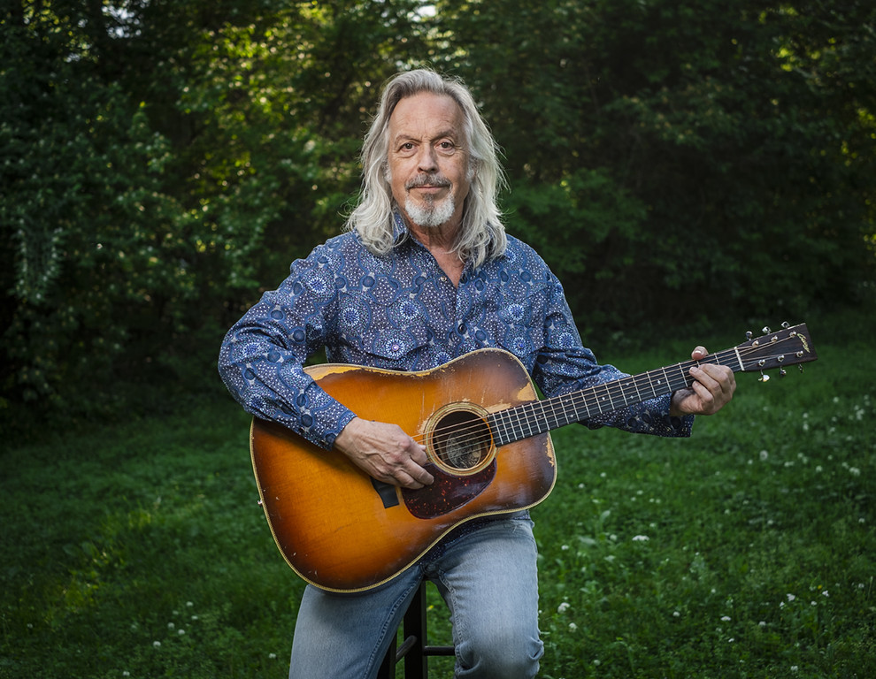 Older man holding acoustic guitar in a green garden