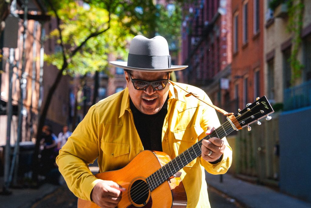 Man in yellow jacket playing guitar on city street