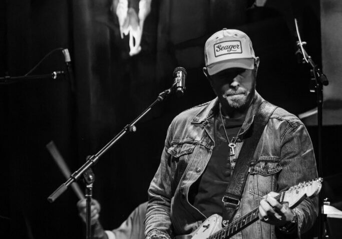 Musician on stage with guitar, bull skull backdrop.