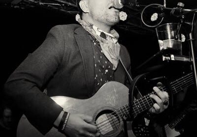 Musician performing on stage with acoustic guitar.