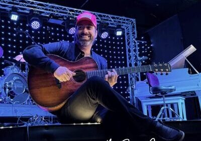 Man playing guitar on stage with festive lights.