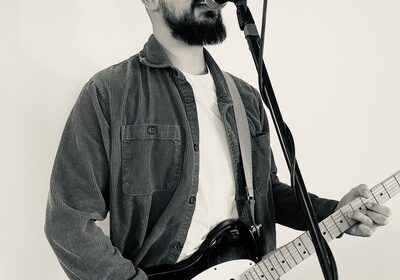 Musician singing and playing electric guitar on stage.