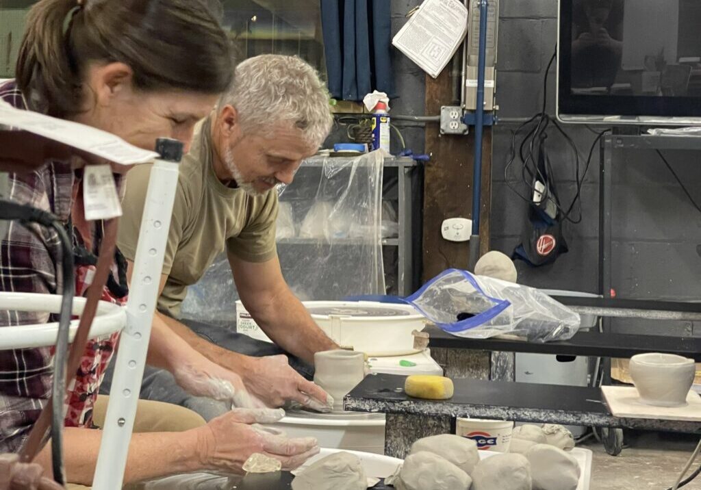 Two people crafting pottery on wheels.