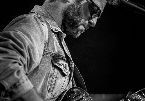 Guitarist performing live on stage in black and white.