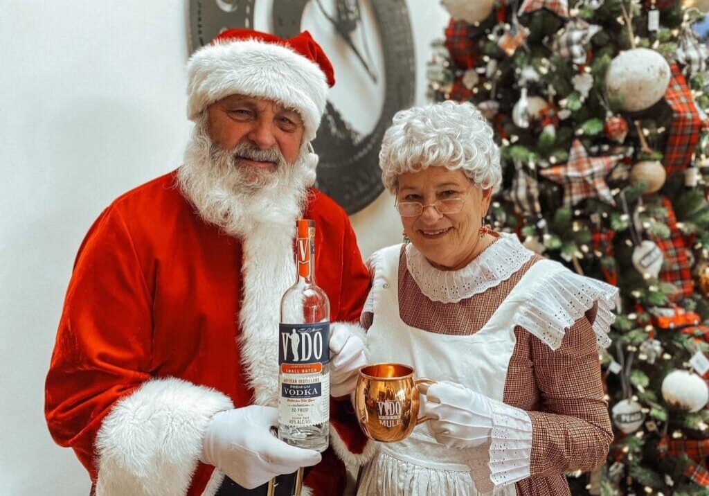 Santa and woman celebrating with drinks by Christmas tree.