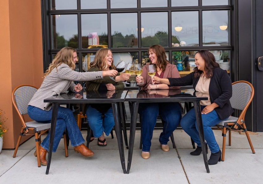 Four women toast with wine outside a storefront