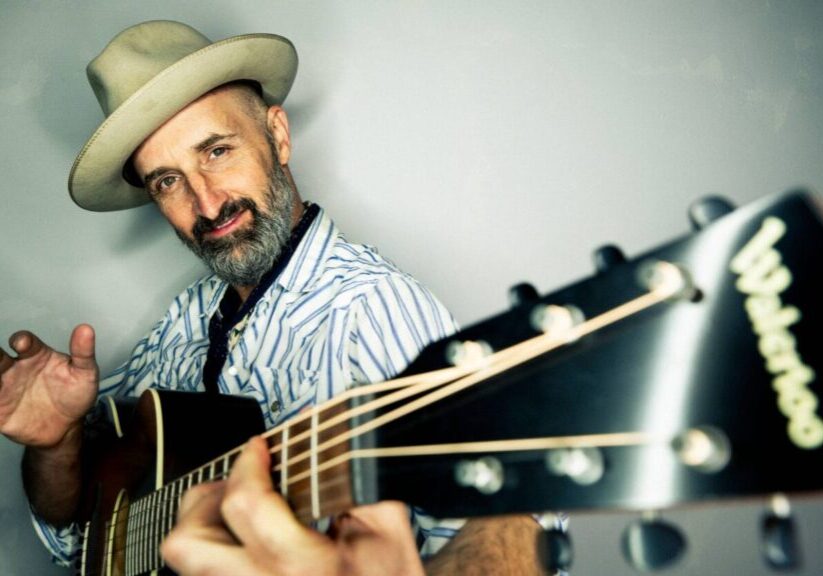 Bearded man playing acoustic guitar in hat